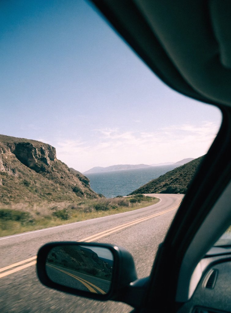 A coastal road curving toward the ocean, seen from a car window